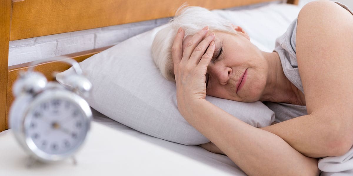 Older-woman-in-menopause-lying-in-bed-with-hand-on-forehead-struggling-to-sleep-with-insomnia